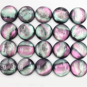 May include: Twenty-one round, iridescent cabochons in shades of purple, pink, and teal. Each cabochon has a swirling, marbled pattern. The cabochons are arranged in a grid pattern, suitable for jewelry making or craft projects.
