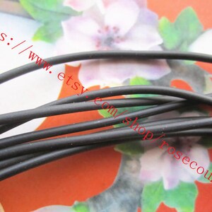 Puede incluir: Un manojo de cord&oacute;n negro fino y flexible con un acabado mate suave. Las hebras est&aacute;n dispuestas en un grupo suelto y superpuesto, mostrando una forma cil&iacute;ndrica consistente a lo largo de todo el material sobre un fondo floral.