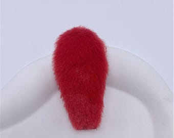 May include: A bright red hair clip featuring a soft, fuzzy, faux fur texture. The accessory has an elongated, rounded shape and is designed to secure hair with a functional metal clip mechanism attached to the underside of the plush red material.
