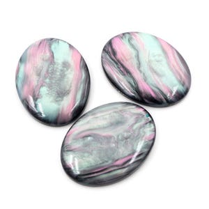 Op de afbeelding: Drie ovale cabochons met een wervelend patroon van roze, grijs en lichtblauw. De gepolijste stenen hebben een glanzende afwerking en zijn geplaatst tegen een witte achtergrond. Deze cabochons zijn geschikt voor het maken van sieraden.