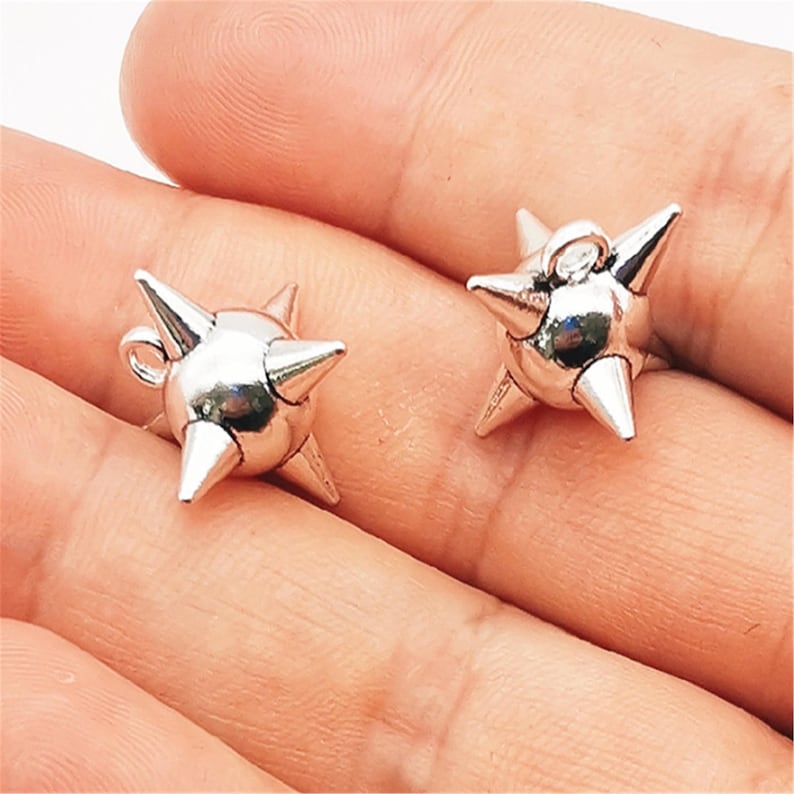 May include: Two silver-colored, spiky stud earrings. Each earring features a central sphere with multiple conical spikes radiating outwards. The earrings are small and appear to be made of a shiny metal.