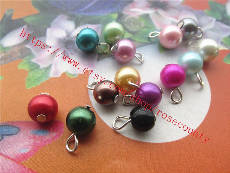 May include: Assortment of colourful pearl beads with silver loops. The beads are in various colours, including red, green, blue, purple, pink, and black.