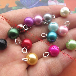 May include: Assortment of colourful pearl beads with silver loops. The beads are in various colours, including pink, green, blue, red, black, and white.