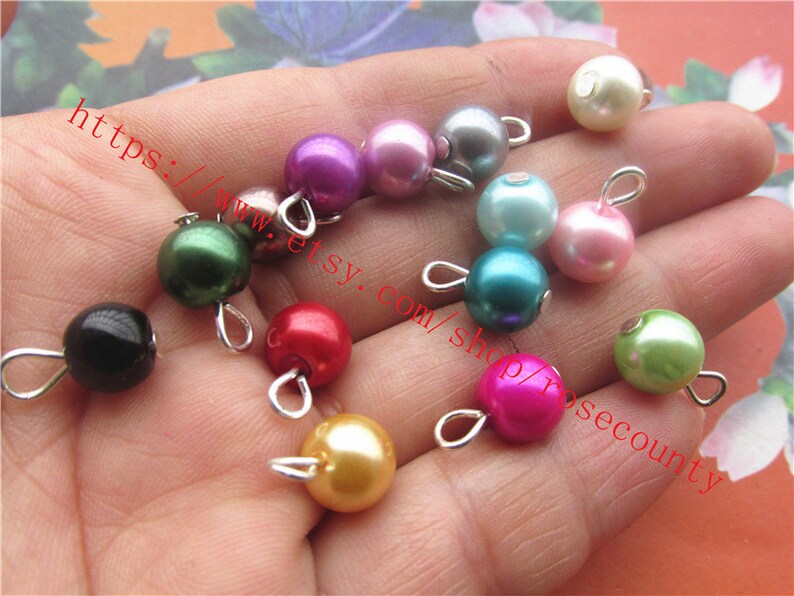 May include: Assortment of colourful pearl beads with silver loops. The beads are in various colours, including pink, green, blue, red, black, and white.