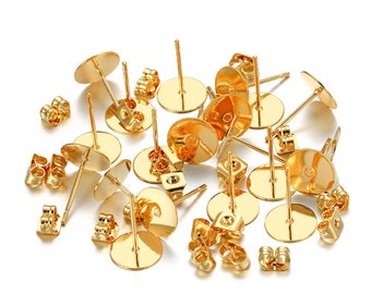 May include: A pile of gold-colored earring findings, including earring backs and earring posts. The findings are scattered on a white background.