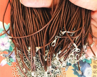 May include: A close-up of a bundle of brown waxed cotton cords with silver lobster clasps. The cords are arranged in a pile, with some of the cords hanging over the edge of the pile. The cords are about 18 inches long.