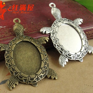 May include: Two turtle shaped metal pendant blanks with oval shaped openings. The turtle on the left is bronze colored and the turtle on the right is silver colored.
