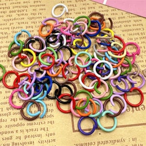 May include: A large assortment of colourful metal jump rings. The rings are various sizes and are arranged in a pile. The rings are a mix of red, orange, yellow, green, blue, purple, pink, brown, black, and white.
