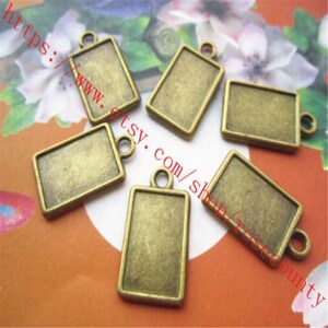May include: Six antique gold-toned metal rectangular pendant charms with a loop at the top for hanging. The charms are blank and ready for personalisation.