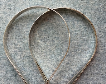 May include: Three silver metal headbands, two larger and one smaller, are arranged on a blue textured fabric background.