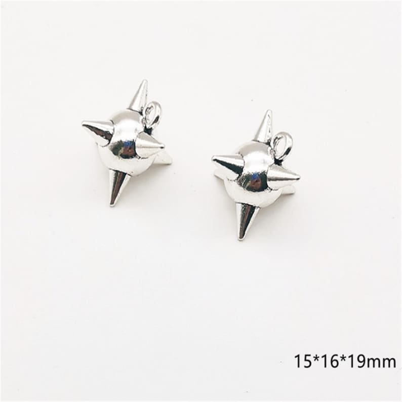 May include: Two silver-colored, star-shaped charms with pointed spikes. Each charm has a small loop at the top for attaching to jewelry. The charms measure 15mm x 16mm x 19mm.