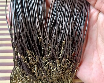 May include: A bundle of brown waxed cords with gold-toned lobster clasps and jump rings. The cords are arranged in a fan shape and are ready to be used for jewelry making.