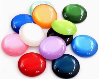 May include: A collection of smooth, round, cabochon-style stones in various colors including red, orange, yellow, green, blue, purple, pink, white, and black. Each stone features a polished, glossy finish with a cat-eye effect that reflects light.