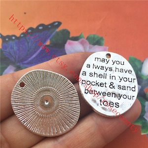May include: Silver charm with a sunburst design on one side and the text "may you always have a shell in your pocket & sand between your toes" on the other side.