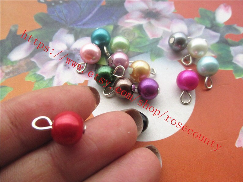 May include: Assortment of colourful pearl beads with silver loops. The beads are in various colours, including pink, red, purple, green, and white.