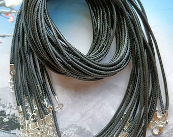 Puede incluir: Un conjunto de collares de cordón trenzado negro con cierres y extensores de cadena plateados. Los cordones están enrollados juntos, y los cierres son visibles en la parte inferior. El fondo es de color azul claro y blanco.