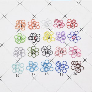 May include: Twenty different colors of jump rings, each color is labeled with a number from 1 to 20. The jump rings are arranged in four rows of five. Each jump ring is approximately 1/2 inch in diameter.