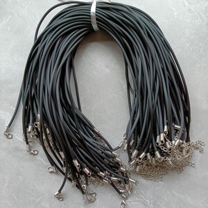 Puede incluir: Un gran manojo de collares de cord&oacute;n de caucho negro, cada uno con un cierre de mosquet&oacute;n de metal plateado y una cadena extensora corta. Los cordones est&aacute;n agrupados en la parte superior con una peque&ntilde;a banda de metal plateado.