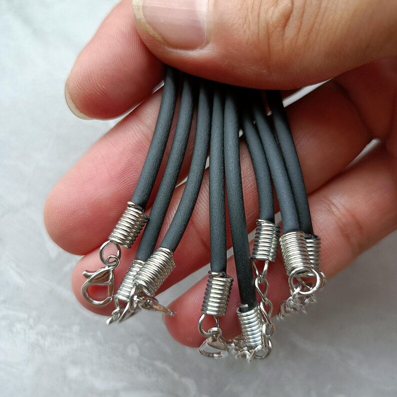 Puede incluir: Un conjunto de cordones negros de caucho para collares con terminales de metal plateado en forma de espiral, cierres de mosquet&oacute;n y cadenas de extensi&oacute;n cortas. Los cordones son lisos, flexibles y de grosor uniforme para joyer&iacute;a.