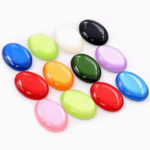 Può includere: Una collezione di cabochon ovali in vari colori, tra cui rosso, arancione, verde, blu e viola. I cabochon hanno una finitura lucida e lucidata e sono disposti su una superficie bianca. Adatti per la creazione di gioielli o altri progetti artigianali.