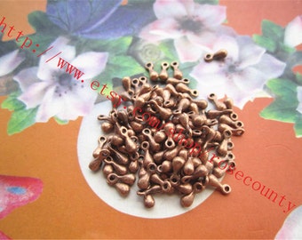 May include: A large pile of copper-colored teardrop-shaped charms with a loop at the top. The charms are scattered on a light brown surface.
