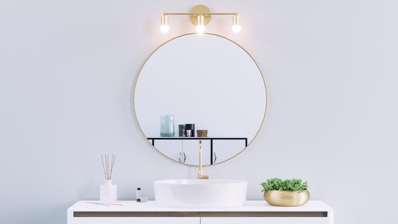 3 Light Mid Century Minimalist Wall Sconce Avon in Brass by Illuminate Vintage Shown Installed Over Bathroom Vanity