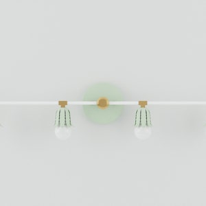 May include: A white and green bathroom vanity light fixture with three light bulbs and a round, green backplate.