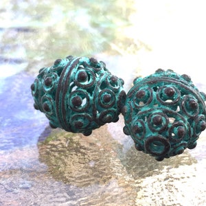 May include: Two teal blue metal beads with intricate, circular designs. The beads have a distressed, aged look.