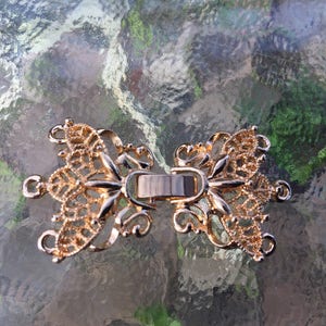 May include: Gold-toned metal clasp with a decorative butterfly design. The clasp is intricately detailed and has a filigree pattern.