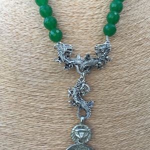May include: A green jade bead necklace with a silver dragon pendant. The pendant features two dragons facing each other with a third dragon hanging below.