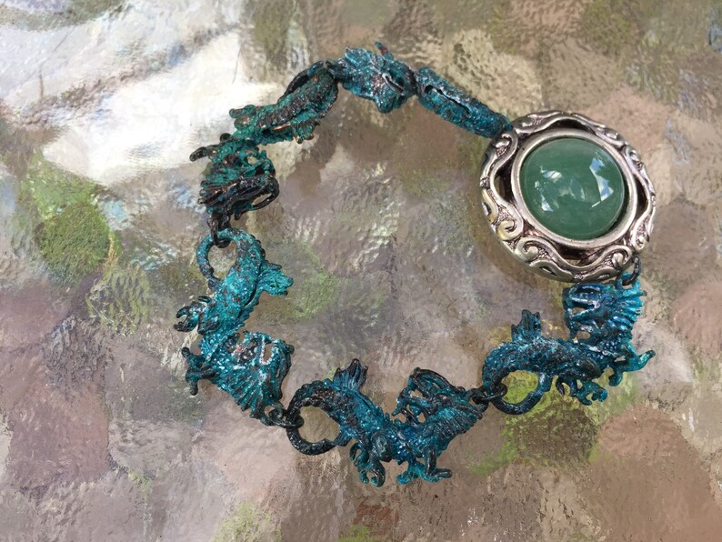 May include: A turquoise blue bracelet with a silver charm featuring a green stone. The bracelet is made of metal and features a design of multiple seahorses.
