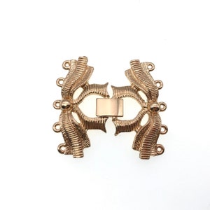K&ouml;nnte beinhalten: Goldfarbener Metallverschluss mit dekorativem Design. Der Verschluss hat auf jeder Seite vier Schlaufen zum Anbringen von Schmuck.