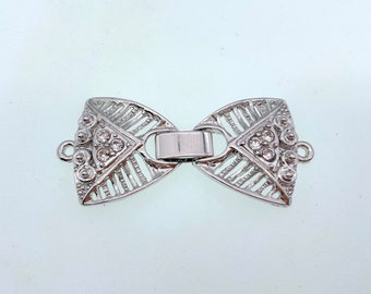 May include: Silver-toned metal clasp with a bow shape and clear rhinestone accents.