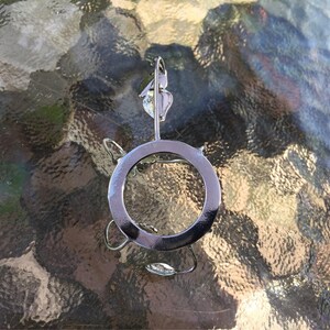 Puede incluir: Un porta anillos de metal plateado con un dise&ntilde;o circular. El soporte tiene un dise&ntilde;o de hoja decorativa en la parte superior.