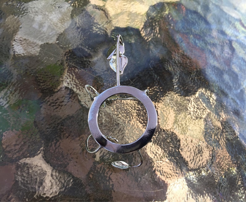 Puede incluir: Un porta anillos de metal plateado con un dise&ntilde;o circular. El soporte tiene un dise&ntilde;o de hoja decorativa en la parte superior.
