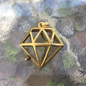 May include: A gold-toned metal pendant shaped like a diamond with a wire cage design. The pendant is open on one side and has a small ball at the bottom.