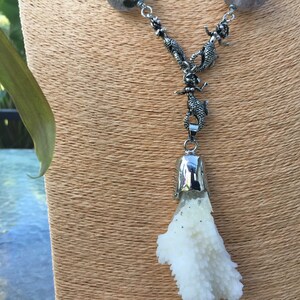 May include: A silver necklace with a white coral pendant. The necklace features a series of silver lizard charms.