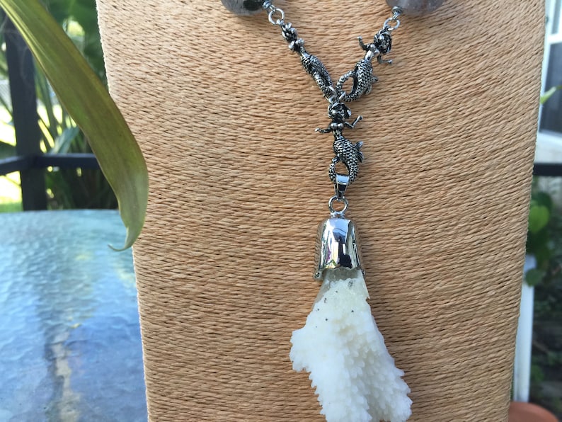 May include: A silver necklace with a white coral pendant. The necklace features a series of silver lizard charms.