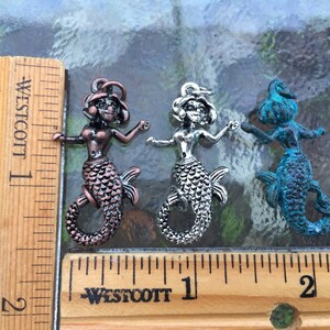 May include: Three mermaid charms in different colors: copper, silver, and blue. The charms are about 1 inch tall and are shown next to a ruler.