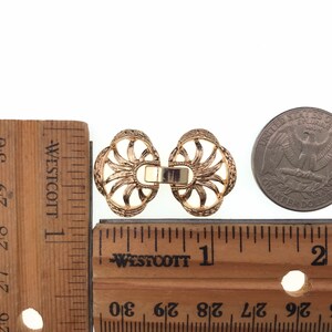 Puede incluir: Dos cierres decorativos de metal dorado con un dise&ntilde;o de rayos de sol. Los cierres miden aproximadamente 2,5 cm de di&aacute;metro y se muestran junto a una regla y una moneda de 25 centavos de d&oacute;lar estadounidense.