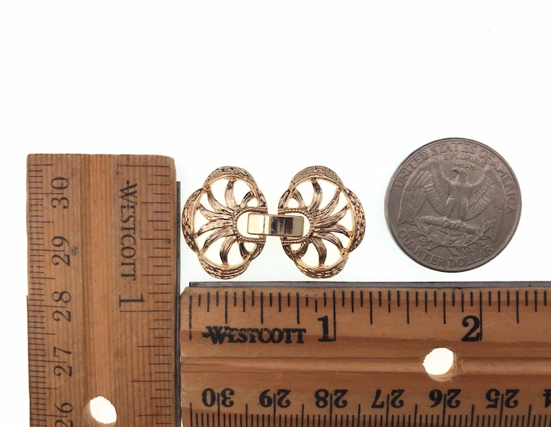 Puede incluir: Dos cierres decorativos de metal dorado con un dise&ntilde;o de rayos de sol. Los cierres miden aproximadamente 2,5 cm de di&aacute;metro y se muestran junto a una regla y una moneda de 25 centavos de d&oacute;lar estadounidense.