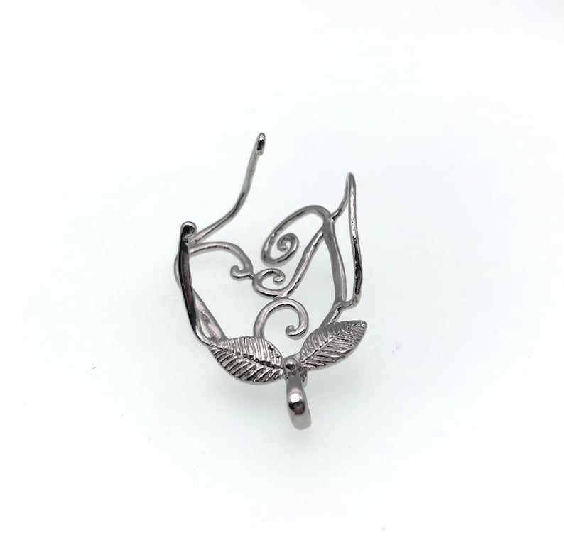 Puede incluir: Anillo de cierre para colgante de metal plateado con un dise&ntilde;o delicado e intrincado que presenta dos hojas y un patr&oacute;n de espiral.