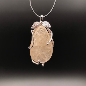 Puede incluir: Un colgante de plata con un cristal transparente en forma de pera engastado en un marco de alambre con dos acentos de hojas.