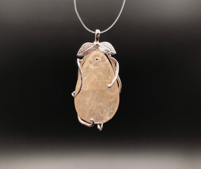 Puede incluir: Un colgante de plata con un cristal transparente en forma de pera engastado en un marco de alambre con dos acentos de hojas.
