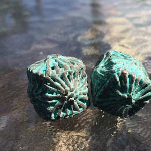 May include: Two teal blue decorative dice with intricate patterns. The dice are made of a textured material and have a slightly aged look.