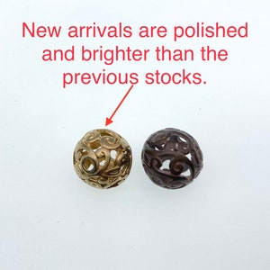May include: Two decorative metal beads with a filigree design. One bead is gold and the other is brown.