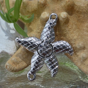 May include: A silver-toned metal starfish charm with a textured surface. The charm has two loops for attaching to jewelry or other crafts.