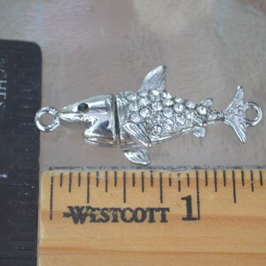 May include: Silver-toned shark charm with clear rhinestones. The charm has a loop for attaching to a necklace or bracelet.