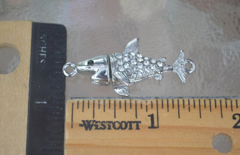 May include: Silver-toned shark charm with clear rhinestones. The charm has a loop for attaching to a necklace or bracelet.