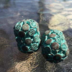 May include: Two teal blue metal beads with a textured, circular pattern. The beads have a distressed, aged look.